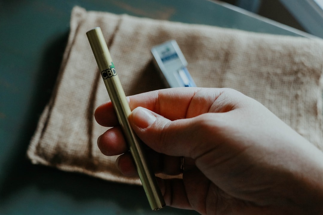 A hand holds a metallic gold CBD vape pen.
