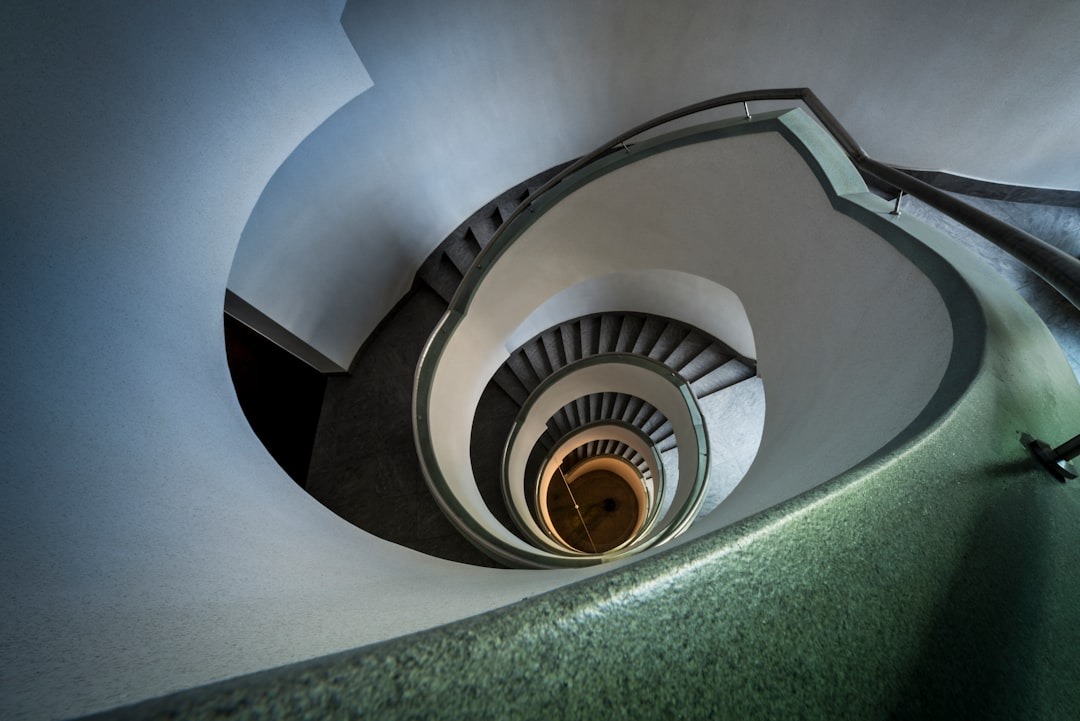 Grey carpeted spiral staircase curving toward a light source.